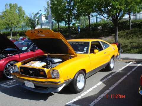 1978 Ford Mustang II - A yellow coupe is parked in a lot with its hood open, revealing the engine compartment.