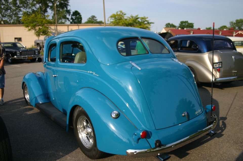 Rear view of a blue hot rod coupe parked next to a tan and blue car