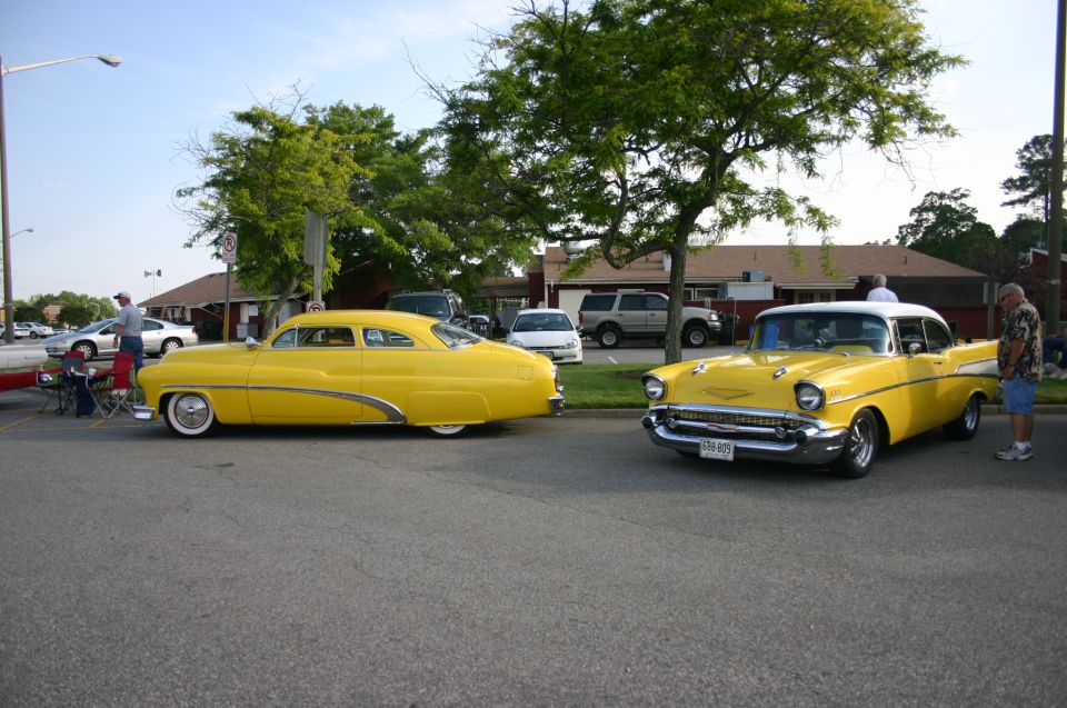 Two yellow classic cars parked outside, one a 50s sedan and the other a 57 Chevy