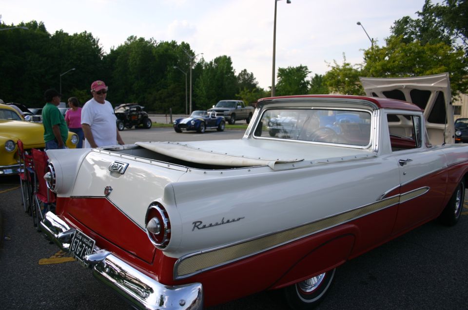 Two-tone red and white pickup truck with a bed cover. People are standing around it