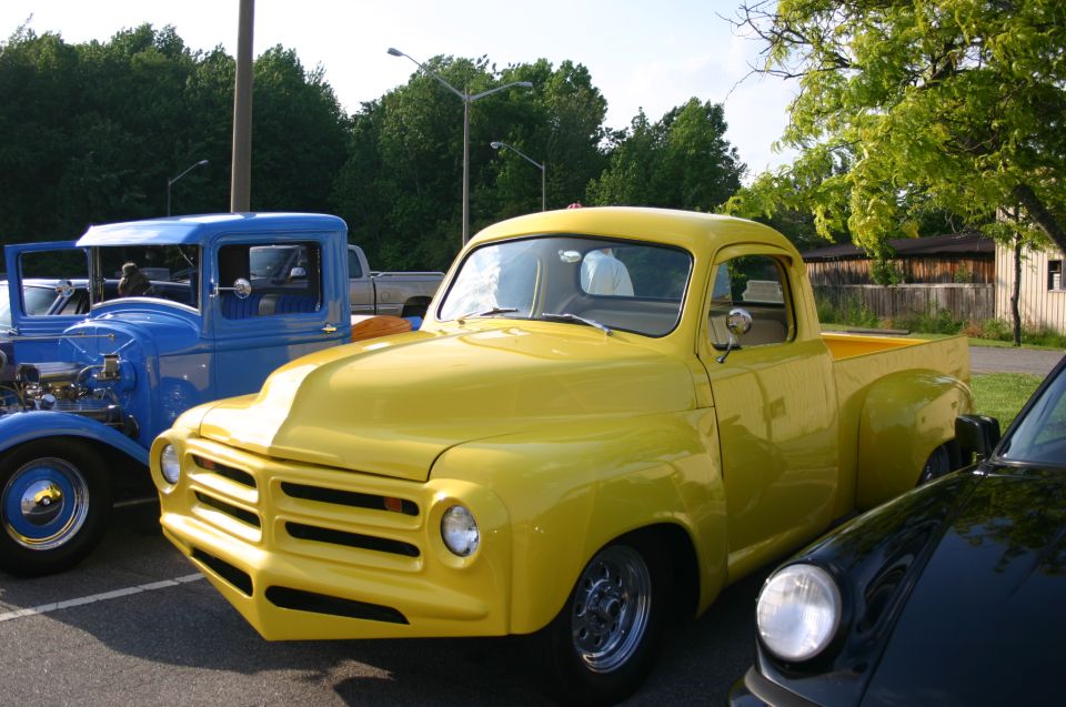 Yellow pickup truck with a custom front end and chrome wheels, parked next to a blue vintage car