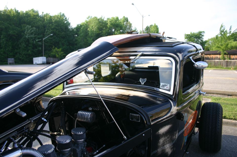 Black hot rod with open hood, surfboard on roof, and exposed engine