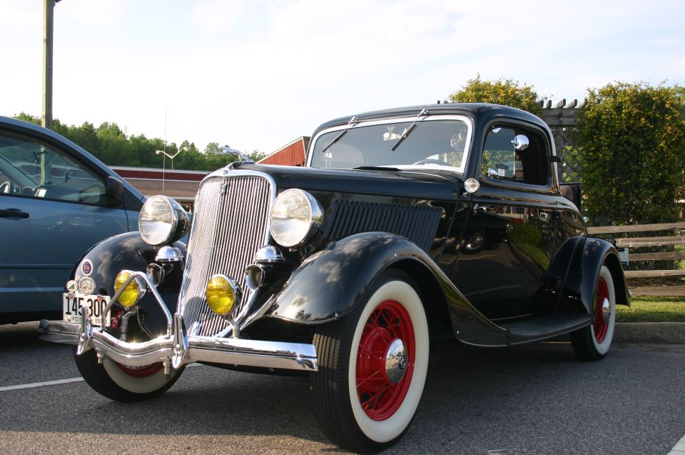 Black hot rod coupe with red wheels and whitewall tires parked outside