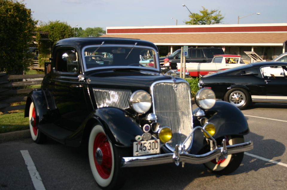 Black 1934 Ford coupe with red wheels and whitewall tires, parked at a car show