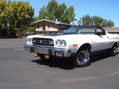 1973 Ford Ranchero - A white coupe utility with a black roof and hood is parked in an asphalt lot with a building in the background.