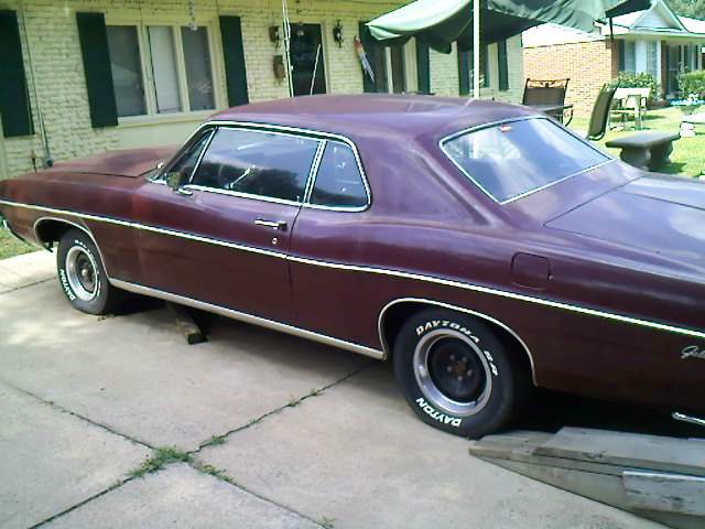 Maroon classic two-door hardtop car with Dayton white-letter tires parked in a driveway by a house