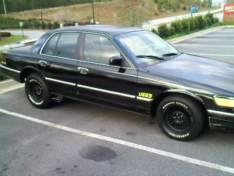 1993 Mercury Grand Marquis - A black sedan with custom wheels and tires is parked in a lot.