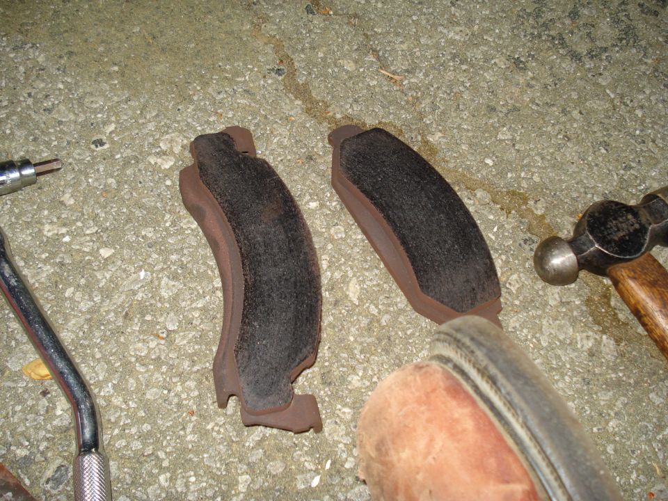 Two brake pads, a hammer, and a wrench on a concrete surface