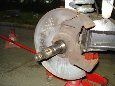 1984 Ford Bronco - Close-up of a vehicle's front brake rotor and hub assembly, supported by red jack stands.