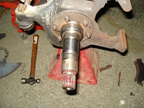 1984 Ford Bronco - Close-up of a vehicle's brake assembly and splined axle shaft, with tools scattered on the concrete floor.
