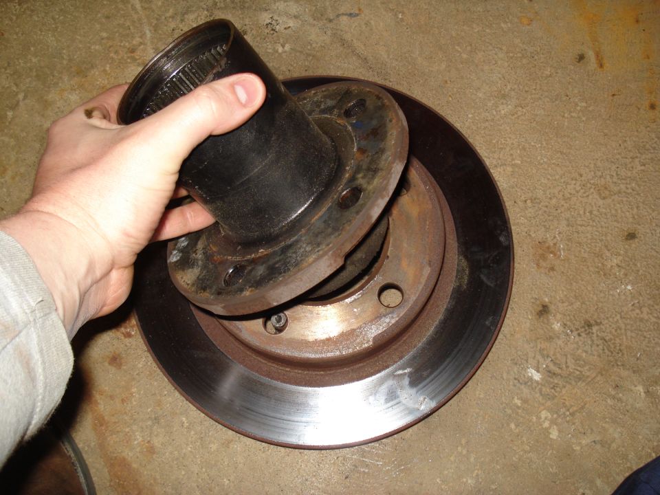 Hand holding a brake rotor and hub assembly. The rotor is rusty. The hub has splines inside