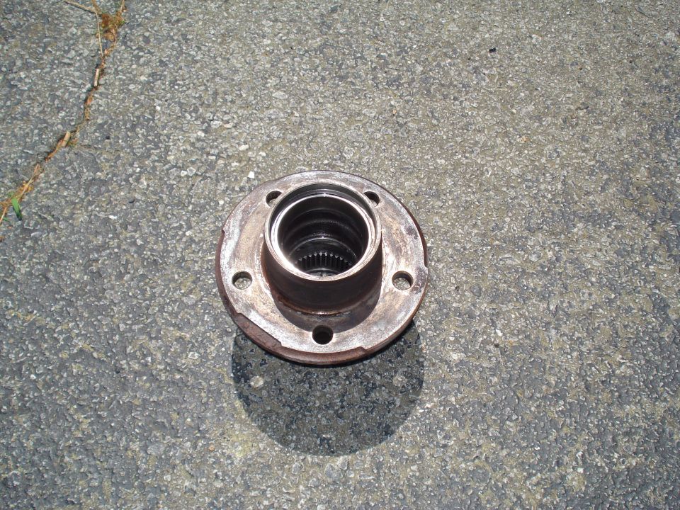 Wheel hub with four bolt holes and splined interior, resting on asphalt
