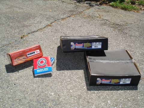 1984 Ford Bronco - Several boxes of automotive parts, including bearings and brake rotors, are laid out on asphalt.