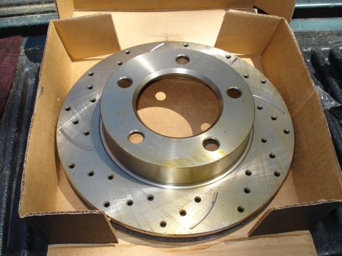 1984 Ford Bronco - A close-up view of a new slotted and drilled brake rotor, packaged in a cardboard box.