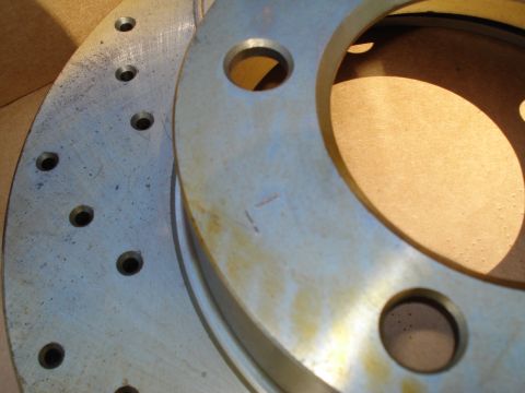 1984 Ford Bronco - Close-up of two brake rotors, one with drilled holes, showing signs of wear and rust.