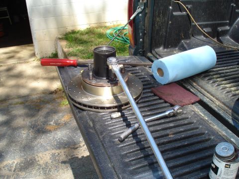 1984 Ford Bronco - Tools and a brake rotor assembly are laid out on the tailgate of a pickup truck, suggesting a repair or maintenance task.