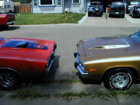1979 Ford Bronco - A red and a gold muscle car are parked side-by-side on a residential street.