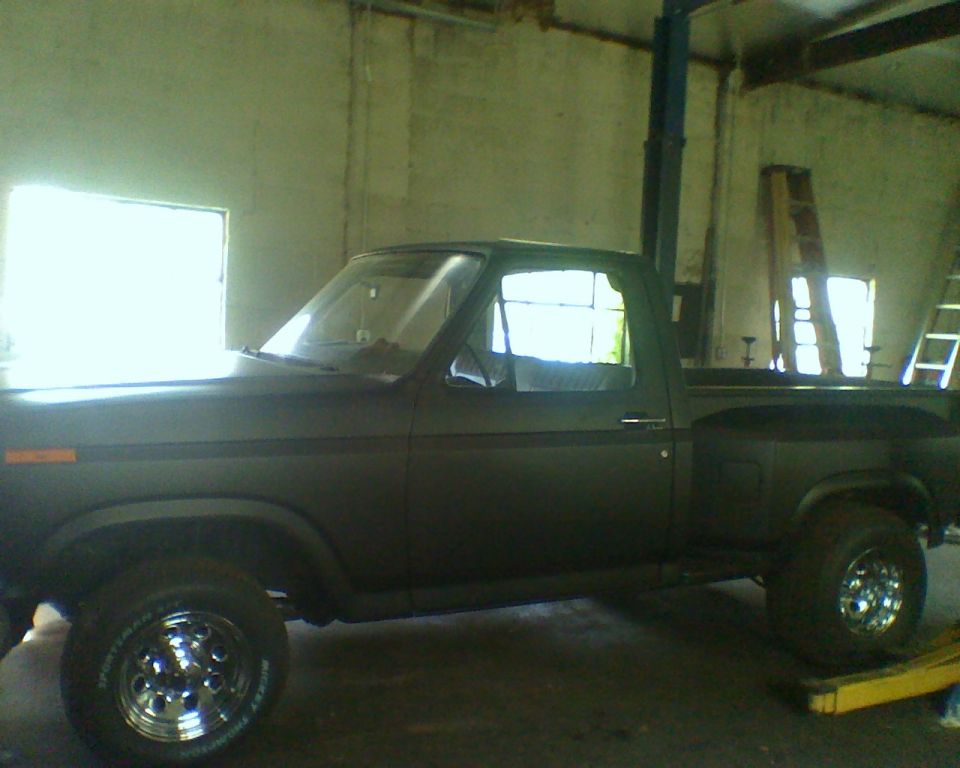 Dark pickup truck, side view, chrome wheels, in a garage with a lift