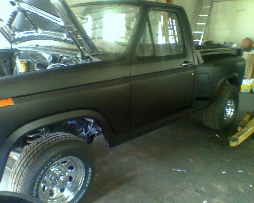 Black Ford F-100 truck with hood open, showing engine bay. Side view