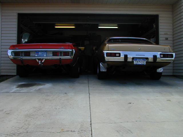 Rear view of a red 1974 Dodge Charger and a gold 1974 Plymouth Road Runner parked side-by-side in a garage