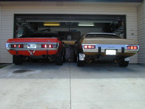 1979 Ford Bronco - Rear view of two vintage muscle cars, one red and one gold, parked side-by-side in a driveway.