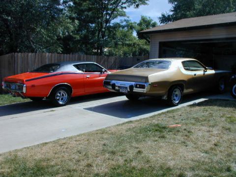 1979 Ford Bronco - Two classic Plymouth muscle cars, a gold Road Runner and a red Charger, are parked in a driveway next to a garage.