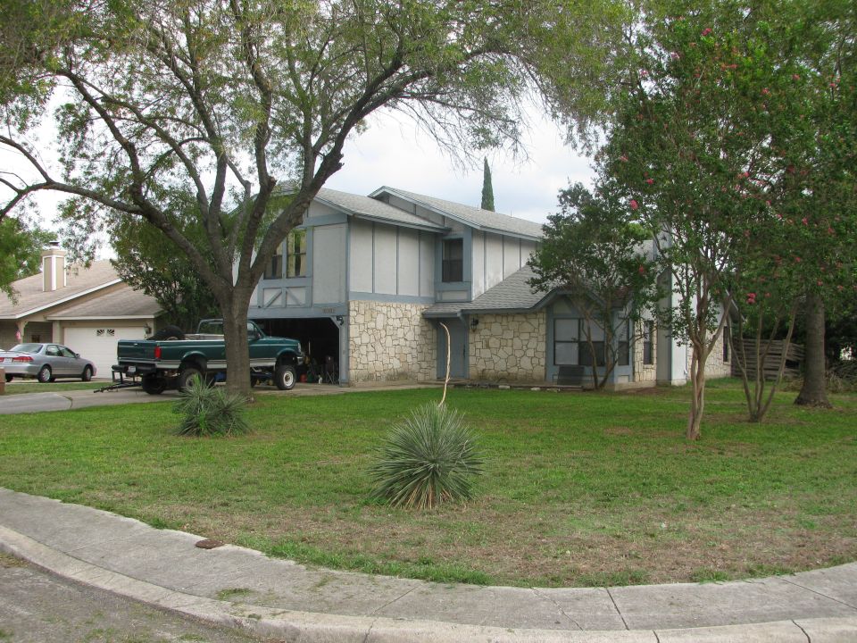 Green pickup truck parked in driveway next to a house. Silver sedan in background