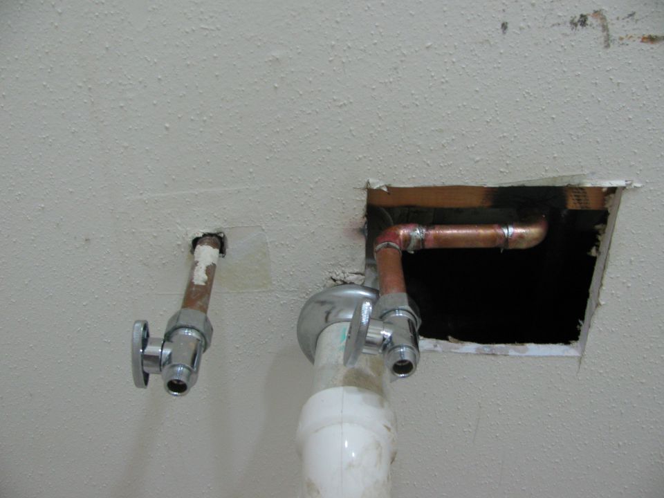Plumbing pipes and shut-off valves protruding from a textured ceiling