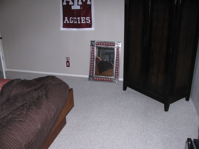 Bedroom with a bed, a dark wardrobe, a mirror, and an Aggies banner
