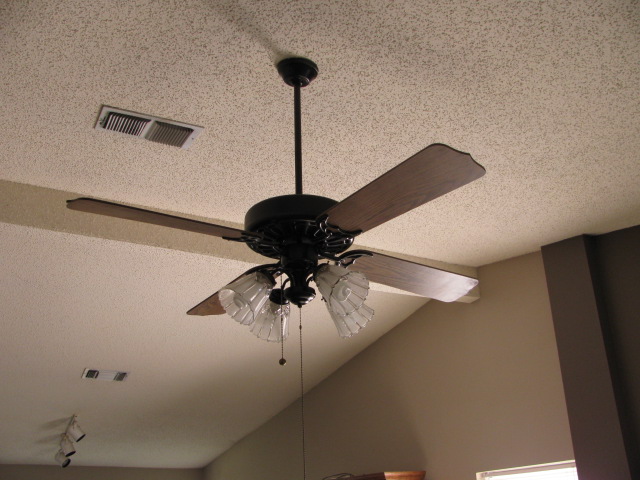 Ceiling fan with dark wood blades and glass light fixtures hanging from a textured ceiling