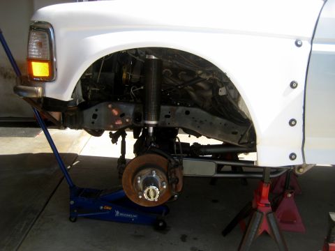 1996 Ford Bronco - Front suspension of a 1996 Ford Bronco, showing the shock absorber and brake rotor, supported by a jack and jack stands.