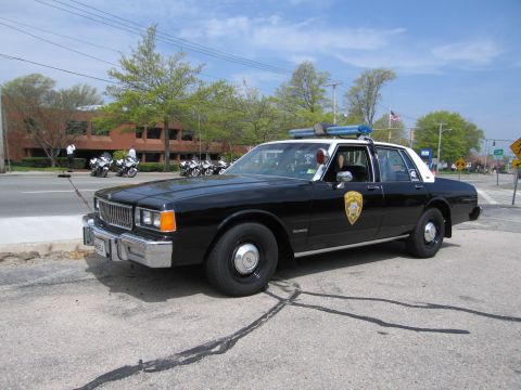 1991 Ford Crown Victoria - A black and white police car is parked on the side of the road with police motorcycles in the background.