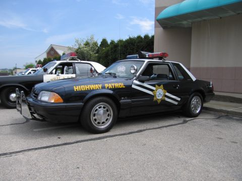 1991 Ford LTD Crown Victoria - side view of a black Fox-body Ford Mustang HIGHWAY PATROL car with a gold star door emblem and roof light bar.