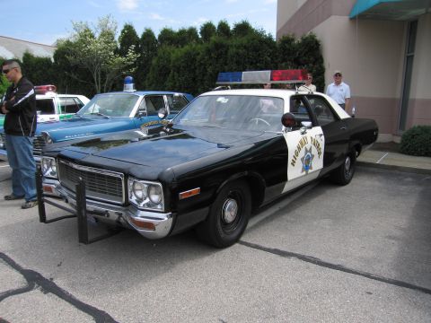 1991 Ford LTD Crown Victoria - black-and-white 1970s Dodge full-size HIGHWAY PATROL sedan with a front push bar and roof beacon parked at a curb.