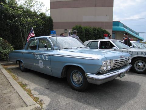1991 Ford LTD Crown Victoria - light-blue early-1960s Chevrolet four-door sedan lettered POLICE, flying a US flag and topped with a roof beacon.