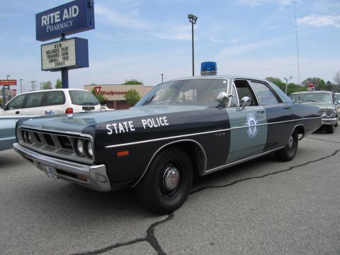 1991 Ford LTD Crown Victoria - black-over-gray vintage State Police four-door sedan with a blue dome light, parked near a Rite Aid pharmacy.