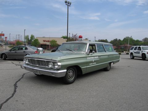 1991 Ford LTD Crown Victoria - green vintage station wagon lettered Stratford Police Radio Patrol with a roof beacon, parked in a lot at a car show.