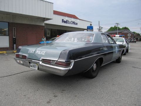 1991 Ford LTD Crown Victoria - Rear three-quarter view of a two-tone vintage State Police sedan with a blue dome light parked outside a FedEx Office.