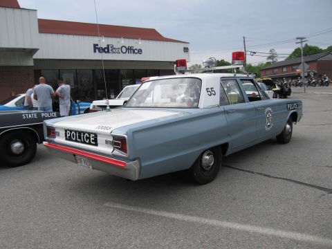 1991 Ford LTD Crown Victoria - Rear view of a light blue vintage police sedan numbered 55 with rooftop lights and a siren, parked outside a FedEx Office.