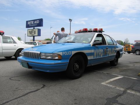 1991 Ford LTD Crown Victoria - blue NYPD-marked Chevrolet Caprice police car with a roof lightbar parked in a lot near a Rite Aid pharmacy.