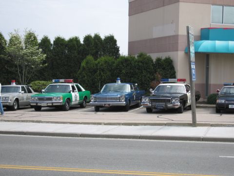 1991 Ford LTD Crown Victoria - row of vintage police cars, including a green-and-white sedan, parked along the curb beside a building.