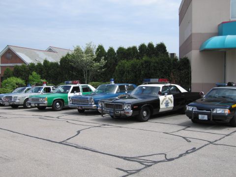 1991 Ford LTD Crown Victoria - lineup of classic police cars parked in a lot, including green, blue and black-and-white highway patrol sedans.