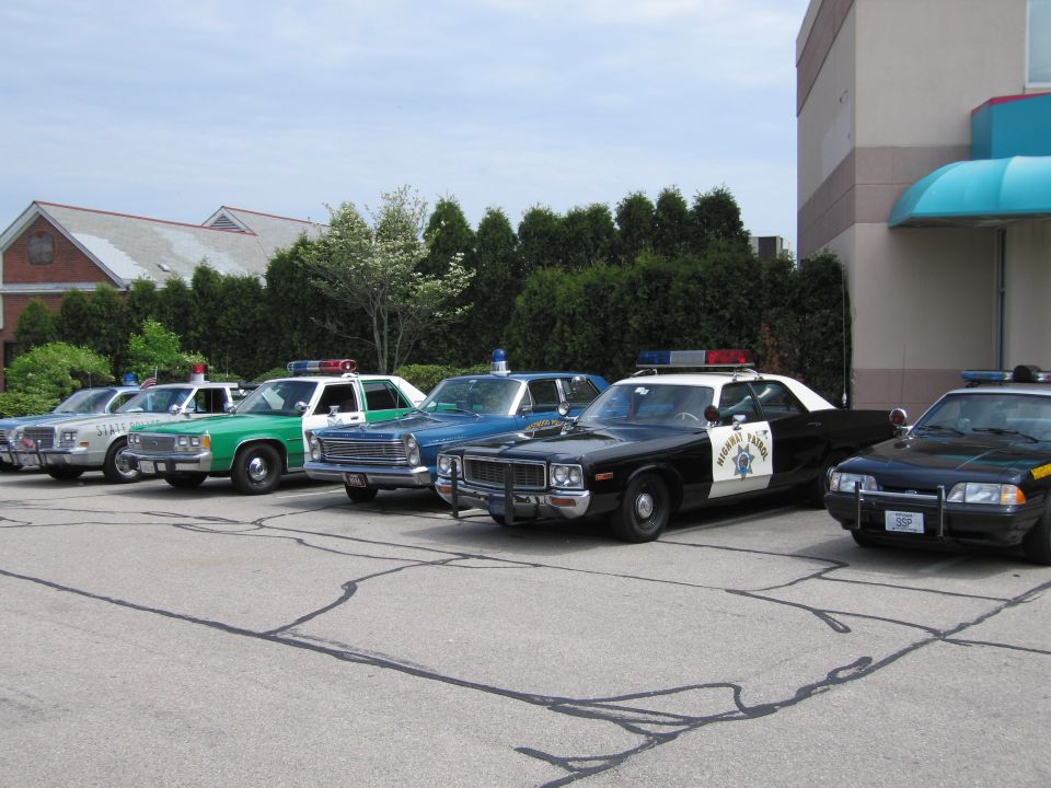 Lineup of classic police cars in a parking lot including a black-and-white