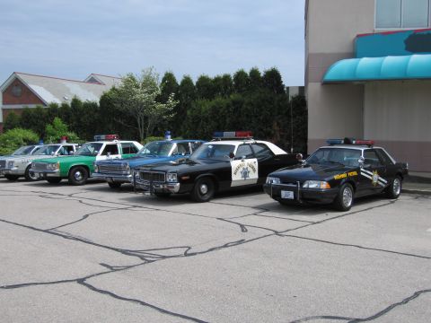 1991 Ford LTD Crown Victoria - row of classic police cars in a lot, including a black-and-white Highway Patrol Mustang and a CHP-style sedan.