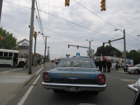 1991 Ford LTD Crown Victoria - Rear view of a blue Westwood Police vintage sedan with plate M986 at a street intersection during a parade.