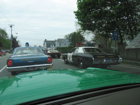 1991 Ford LTD Crown Victoria - blue Westwood Police sedan beside a black-and-white Highway Patrol car on a residential street during a parade.