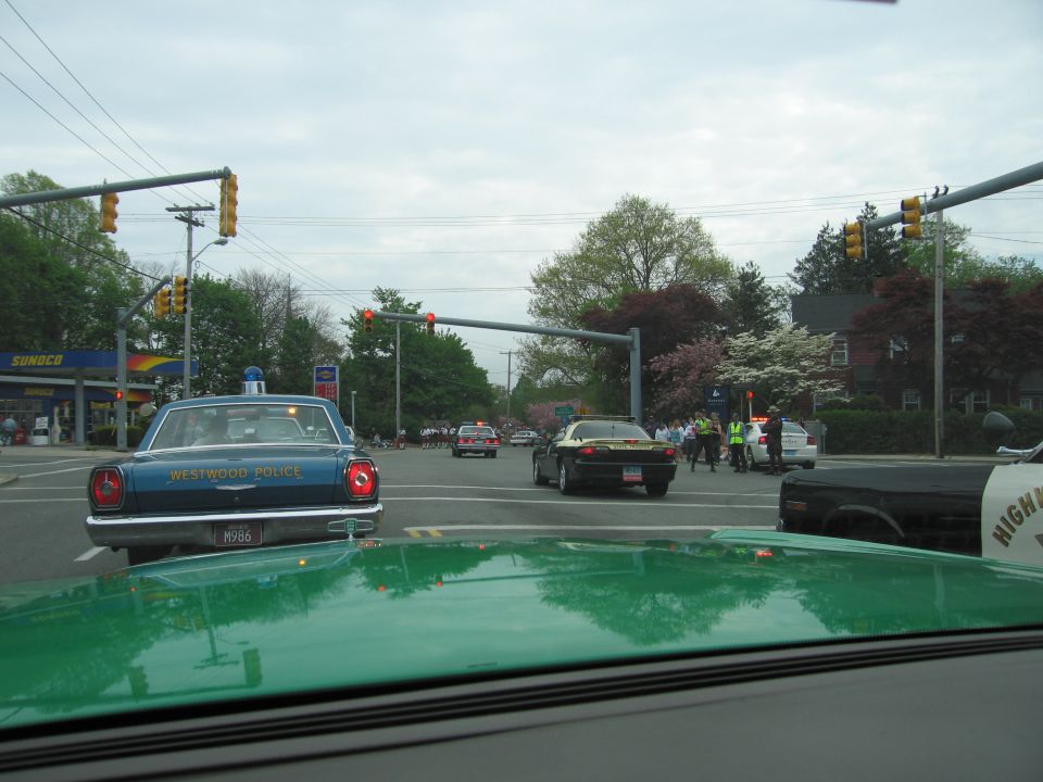 Blue Westwood Police vintage sedan at a town intersection seen over a green hood