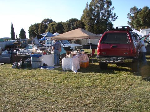 1973 Ford Ranchero - A busy outdoor swap meet displays various car parts and multiple vehicles under tents.