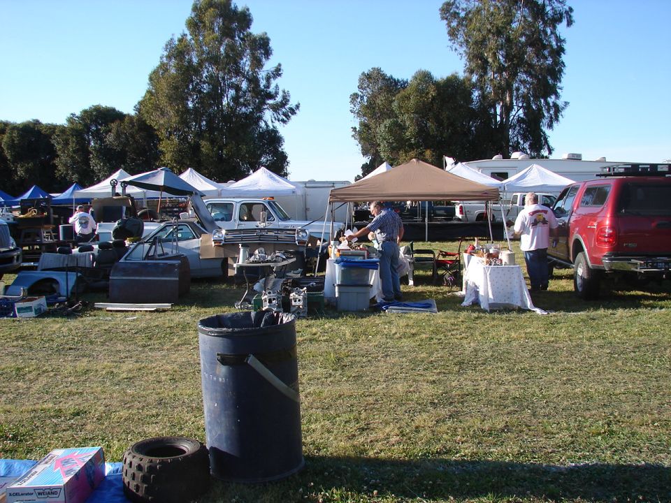 Outdoor swap meet with tents, car parts, and people browsing