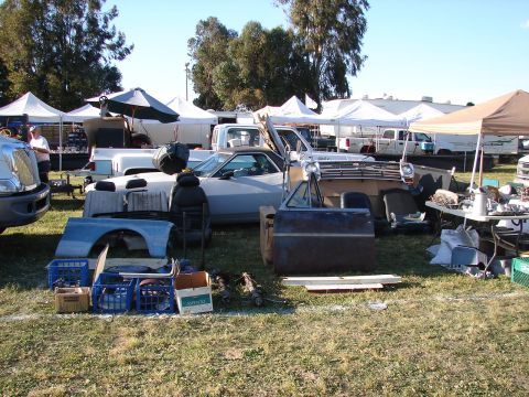 1973 Ford Ranchero - Various car parts are laid out on the grass at an outdoor market, with several vehicles and tents in the background.